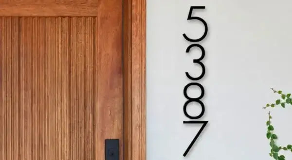 Modern house numbers on a white wall next to a wooden door