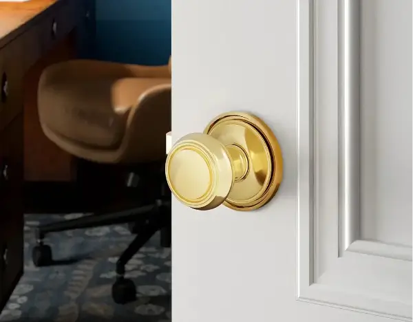 Gold door knob on a white door with a desk and chair in the background