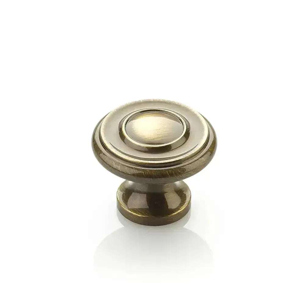 The Schaub Traditional Stepped Round Cabinet Knob in Antique Brass finish.