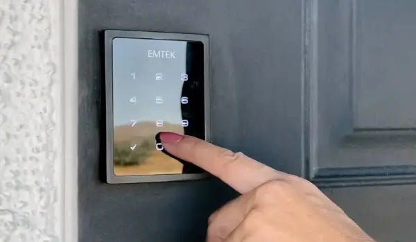 Person using a digital door lock with 'Emtek' branding on a door.