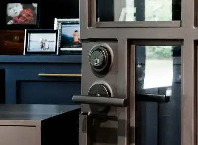 Close-up of a metallic door handle and lock with a desk and framed photos in the background.