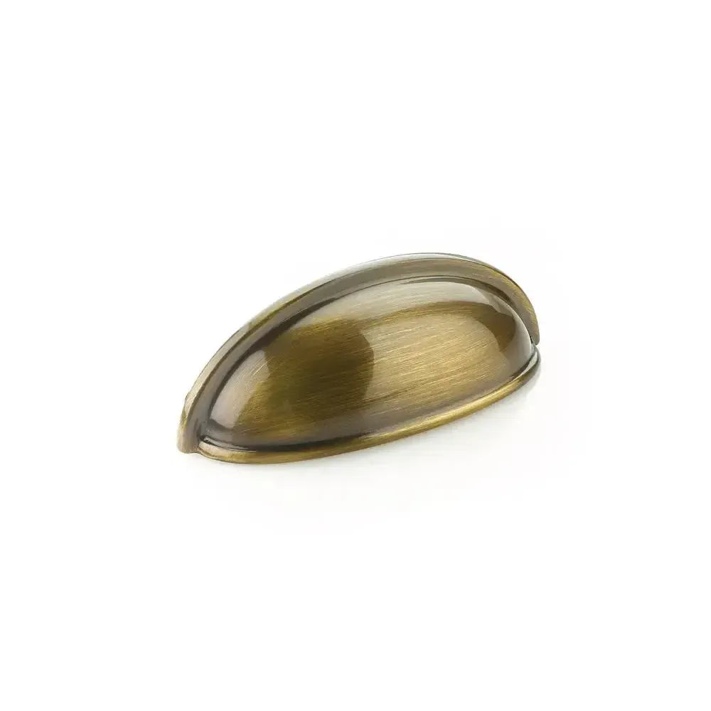 The Schaub Traditional Cup Cabinet Pull in Antique Brass finish.
